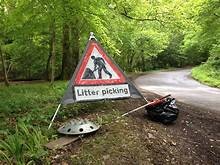 red triangular warning sign with the words litter picking by the side of a rural road